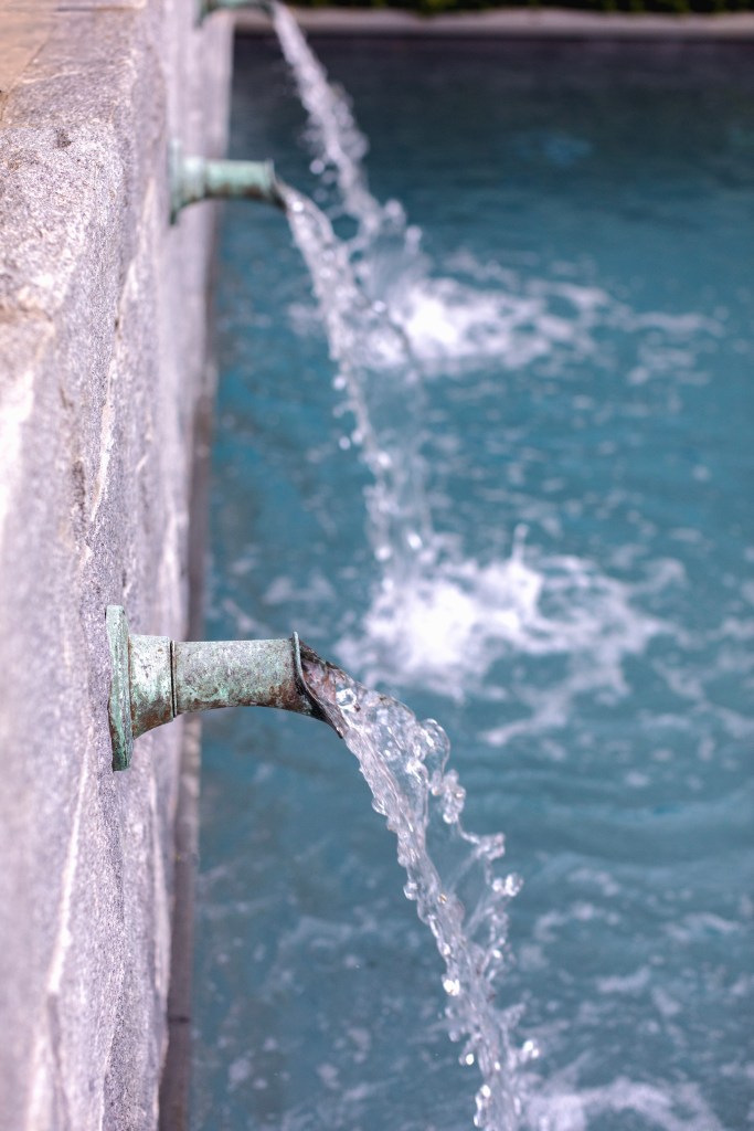 Water flowing from bronze spouts into a swimming pool with rippling blue water.