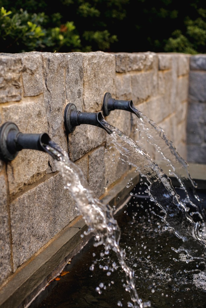 Close-up of three water spouts flowing into a stone basin