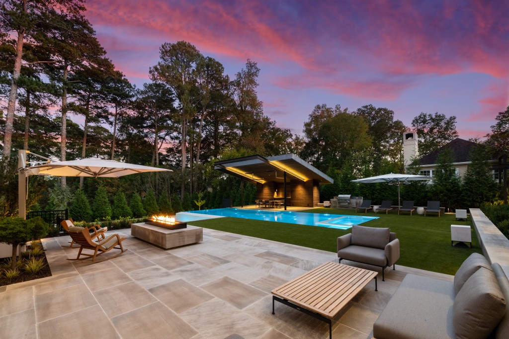 Modern outdoor patio with a swimming pool, lounge chairs, and a fire pit at sunset.