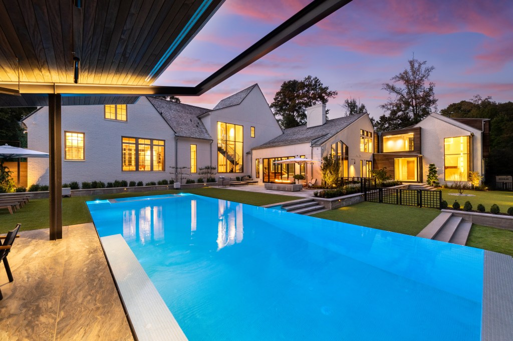 Modern luxury home with a swimming pool and landscaped yard at sunset.