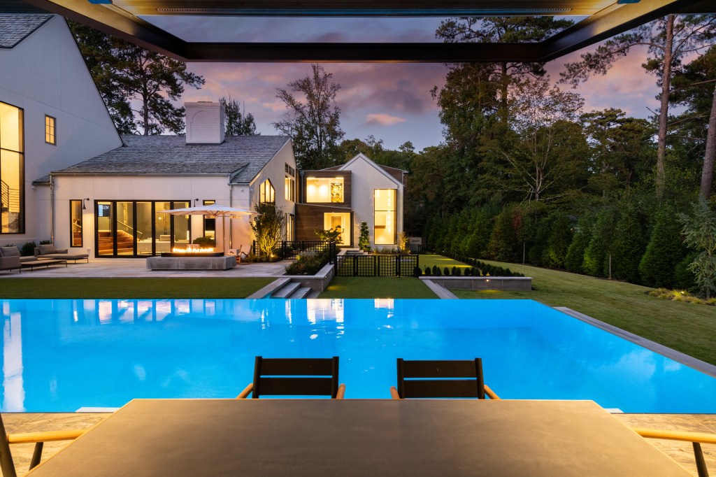 A modern outdoor space with a clear swimming pool in the foreground, overlooking a manicured lawn and contemporary home at dusk.