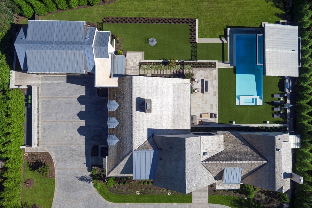 Aerial view of a modern residential property featuring multiple structures, manicured lawns, a swimming pool, and a paved driveway.