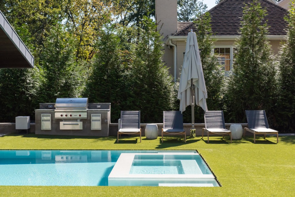 Outdoor area featuring a swimming pool, lounge chairs, a grill, and a patio umbrella surrounded by greenery.