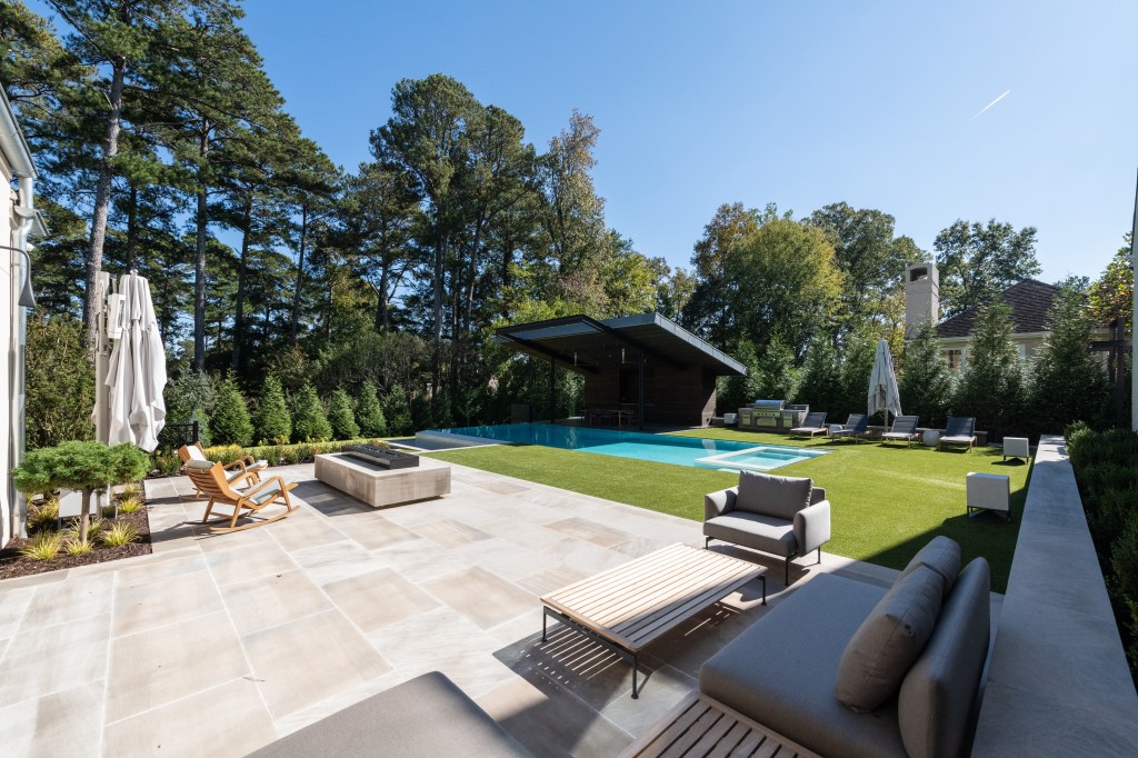 Spacious outdoor pool area featuring a modern pool, lounge chairs, and shaded seating; surrounded by lush trees and landscaping.