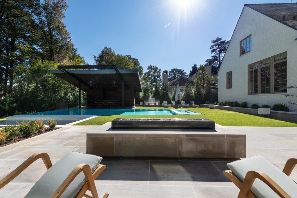 A serene backyard featuring a swimming pool, a modern pavilion, and well-maintained landscaping, capturing a bright, sunny day.