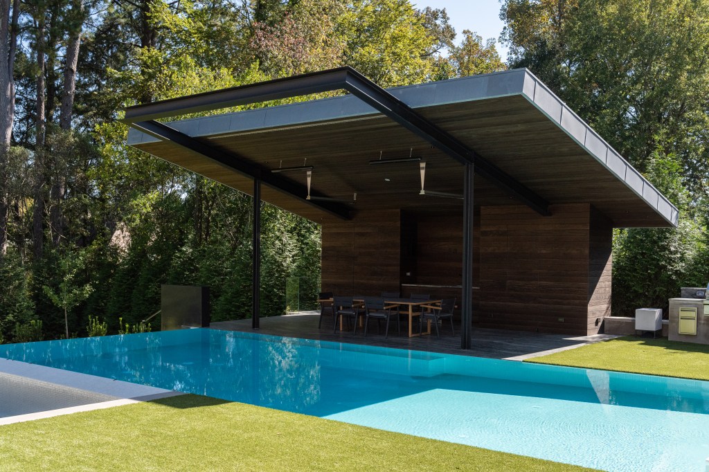 Modern outdoor patio with a pool and a covered seating area surrounded by greenery.