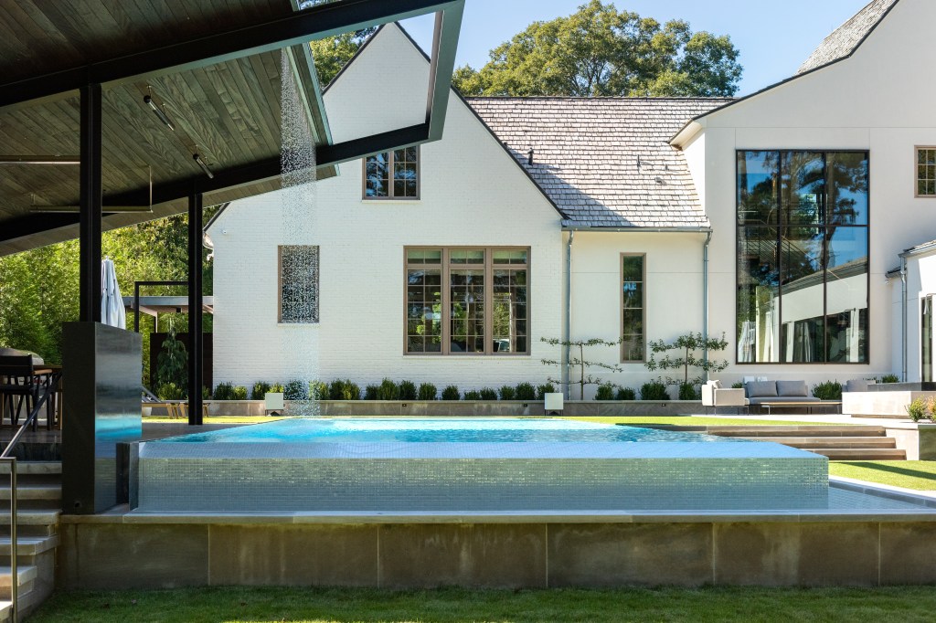 Modern outdoor pool area with a waterfall feature, surrounded by well-manicured grass and contemporary architecture.